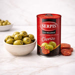 Can of Serpis green olives with chorizo next to a bowl of olives on a white surface