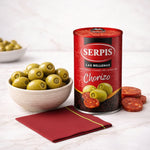 Can of Serpis green olives with chorizo next to a bowl of olives on a white surface