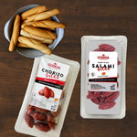 Two packages of Goiko Salami Bites and Chorizo Bites on a wooden surface with bread sticks.