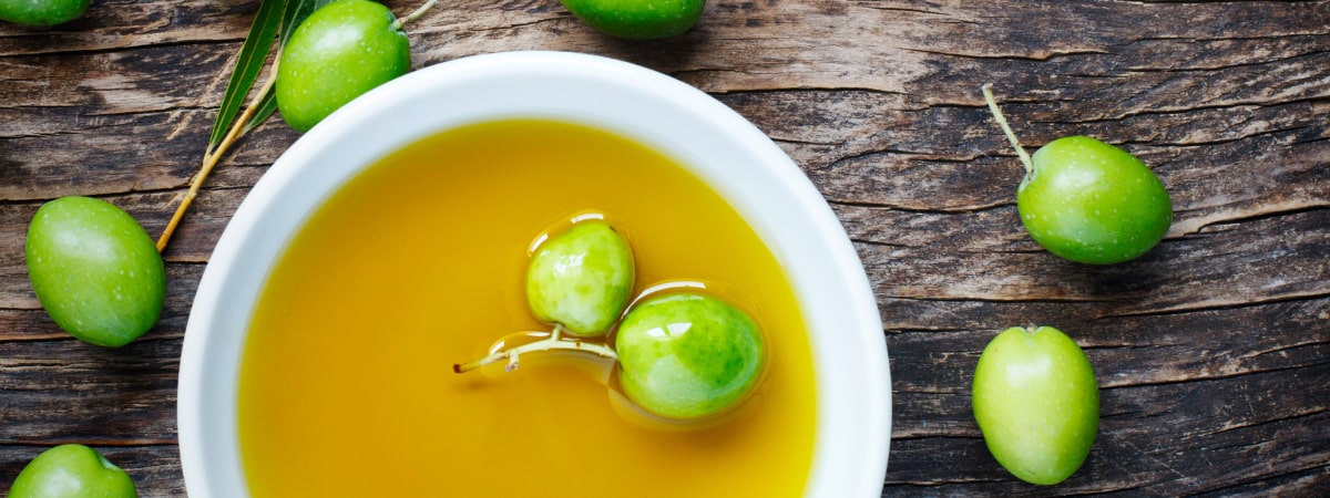 Green fruits on a wooden surface with a bowl of yellow liquid.