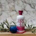Bottle of Morellana Picuda olive oil with a glass on a wooden surface with plants.