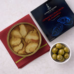 Oysters in a can with a box labeled 'La Mar de Tazones' and a bowl of green olives on a light surface.