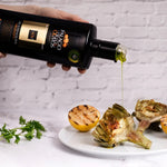 Olive oil being poured from a bottle onto roasted vegetables on a white plate.