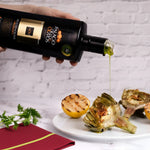 Olive oil being poured from a bottle onto roasted vegetables on a white plate.