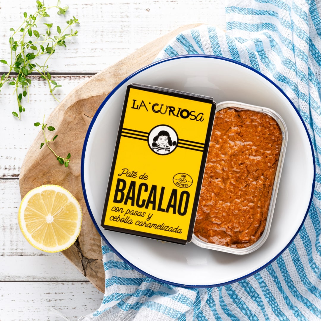 La Curiosa cod paté can surrounded by a lemon and a plant.