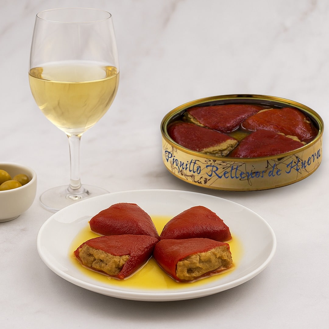 Red stuffed peppers on a white plate with a glass of white wine and a can of red peppers in the background.