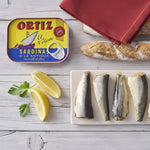 Ortiz sardines can with sardines, bread, and lemon on a wooden surface