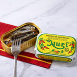 Open can of sardines with a Nuri brand pack on a marble surface