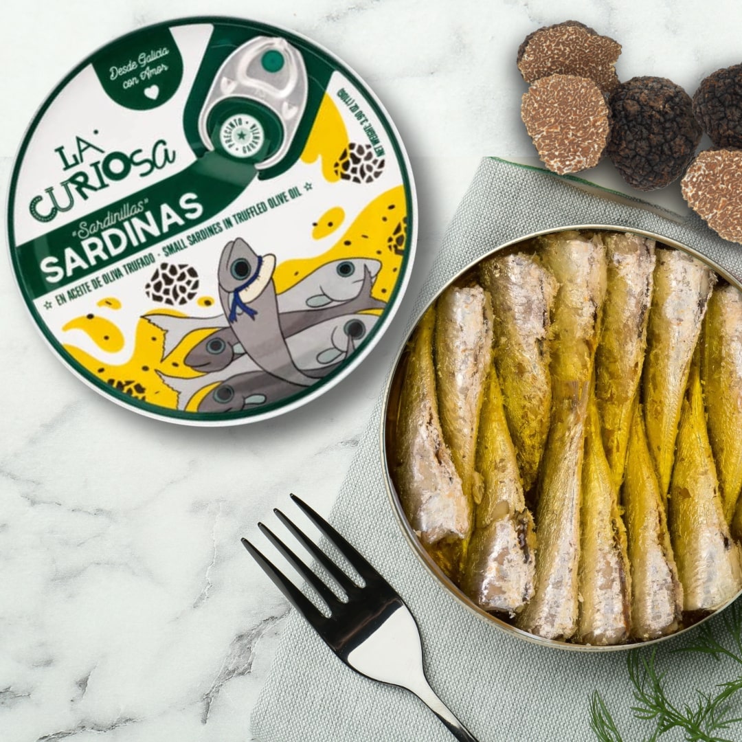 Open can of sardines in truffle oil with 'La Curiosa' packaging on a marble surface.