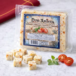 Packaged cheese with 'Don Andres' label on a white surface with sliced tomatoes and cheese cubes.