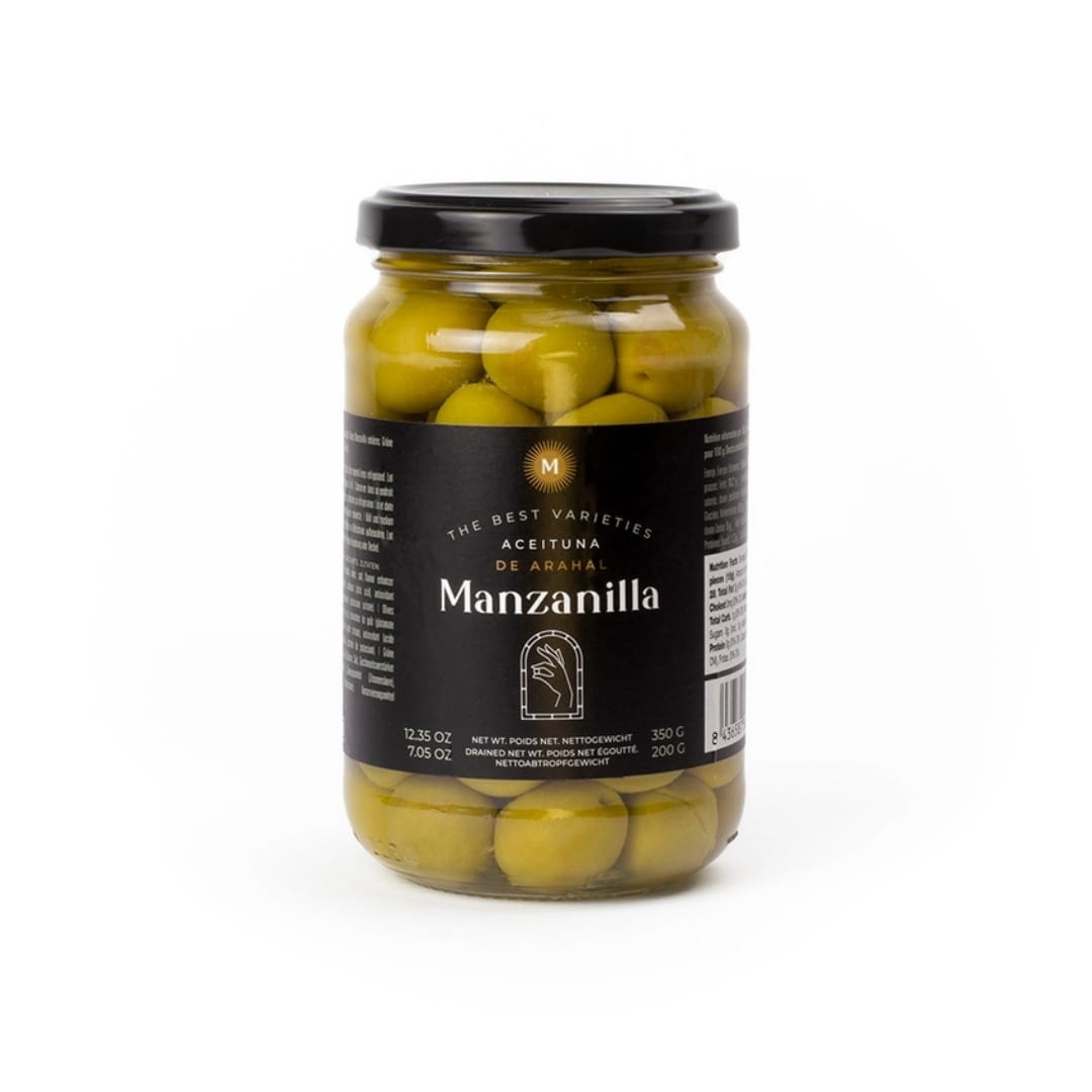 A glass jar of Manzanilla preserved green olives with a black lid and black label, set against a plain white background.