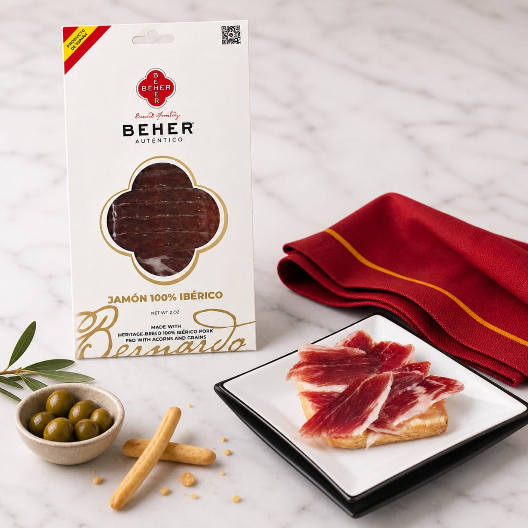 Beher jamón packaging with sliced ham on a plate, olives, and bread sticks on a marble surface.