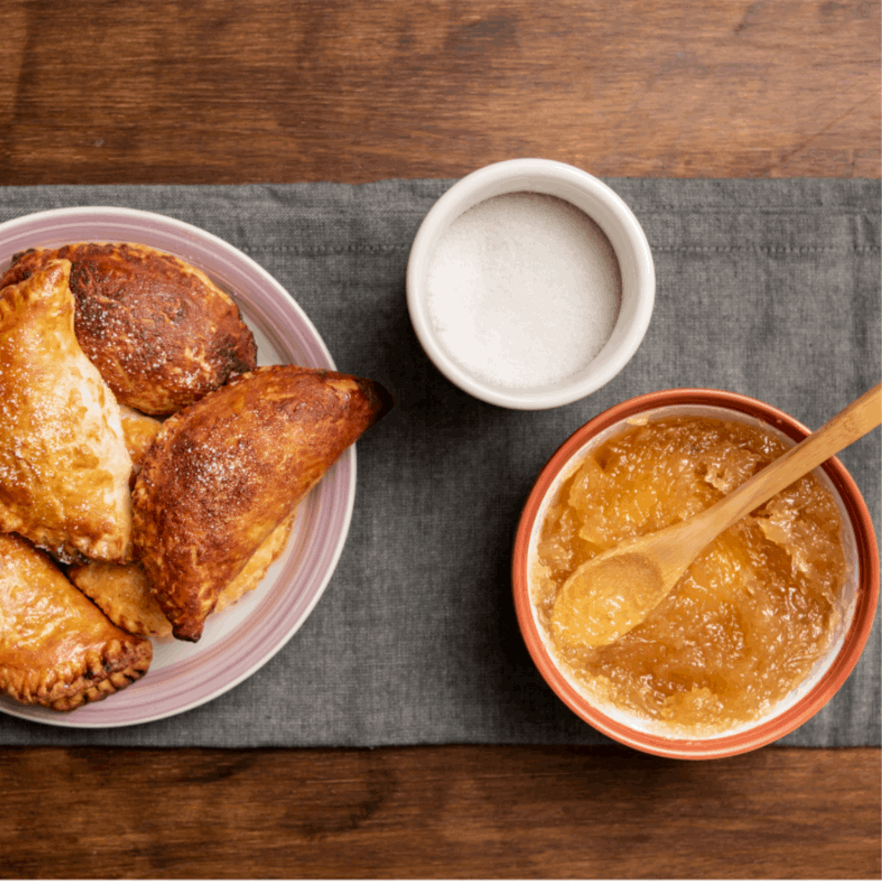a plate with three empanadas and a bowl with a orange paste on a wooded table