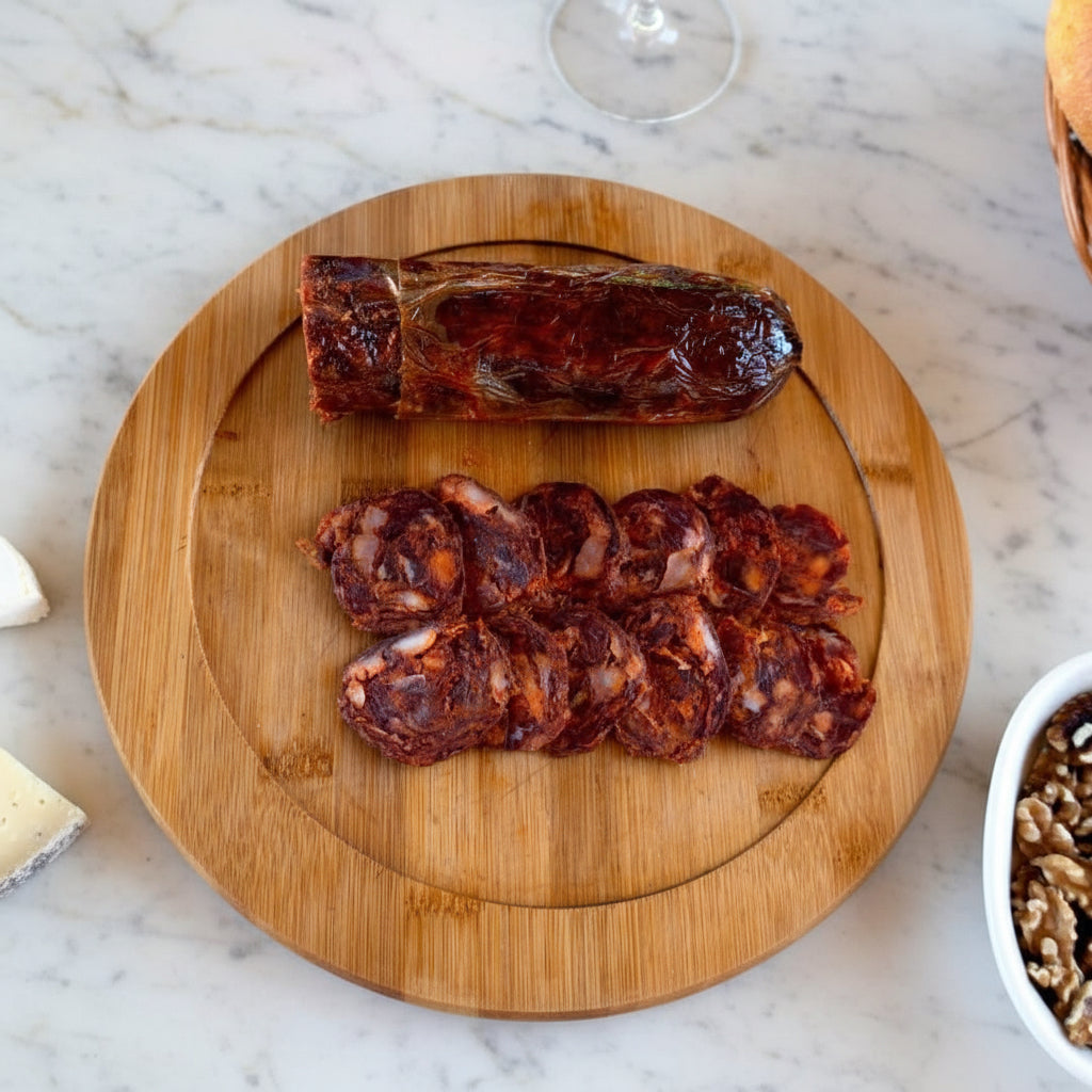 Wooden cutting board with sliced iberico chorizo on a red surface