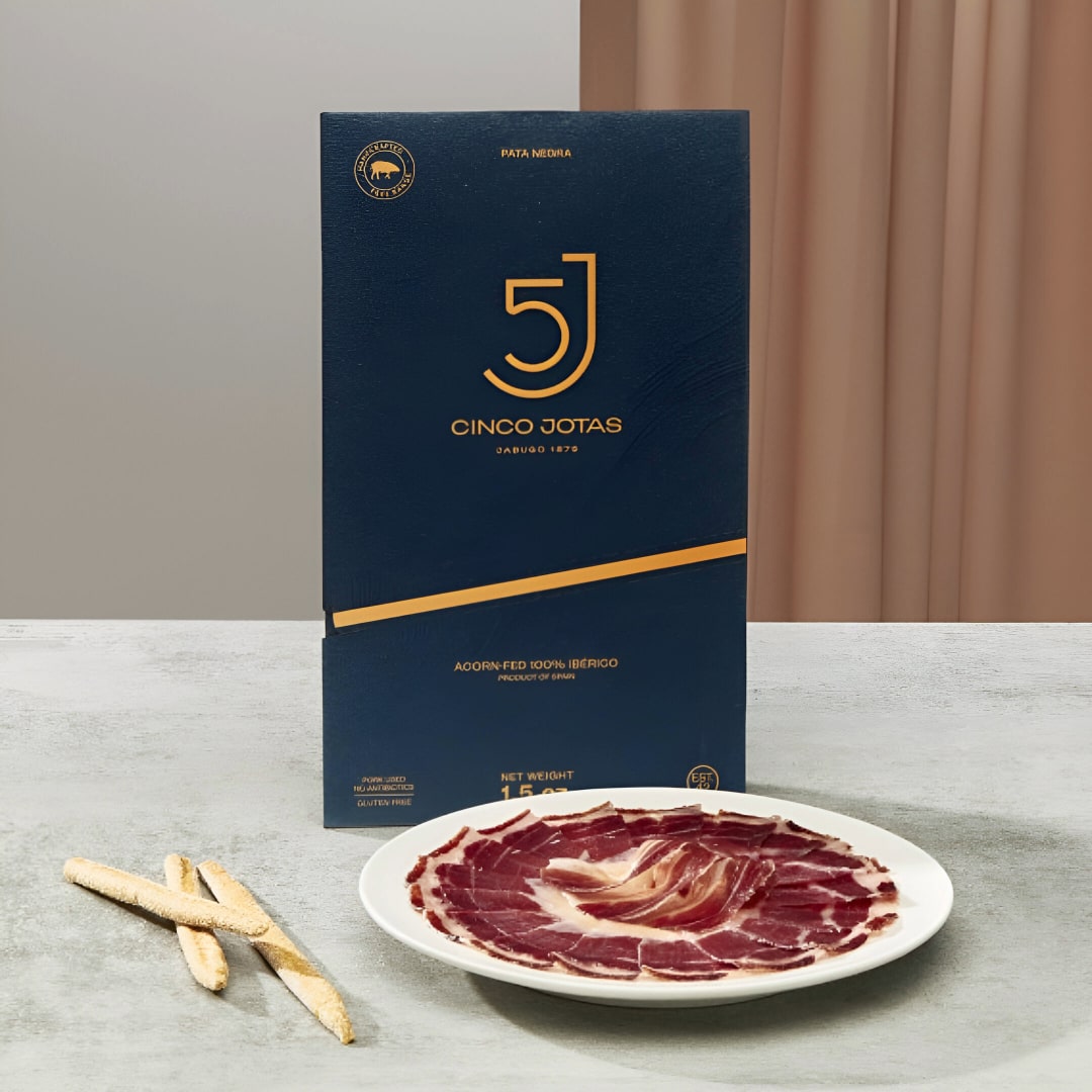Cinco Jotas packaging with a plate of sliced iberico ham on a neutral background