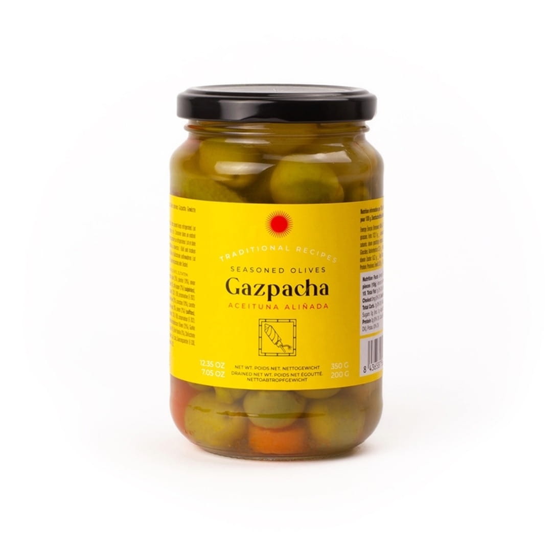 A glass jar of Gazpacha seasoned olives on a clean white background. The jar has a black lid and a bright yellow label with the brand name Gazpacha in black text.