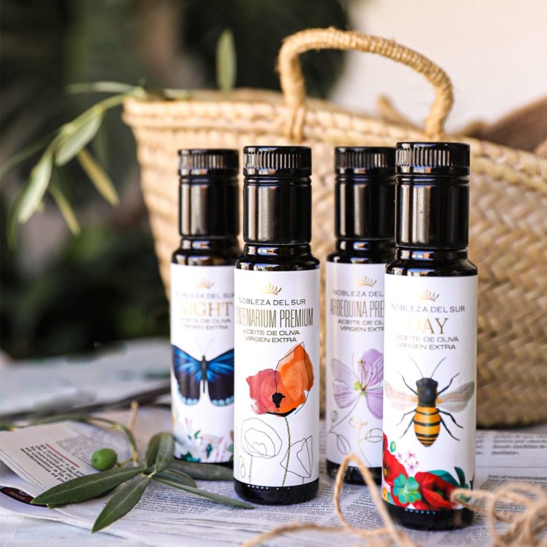 Four bottles of olive oil with decorative labels on a table with a woven basket in the background.