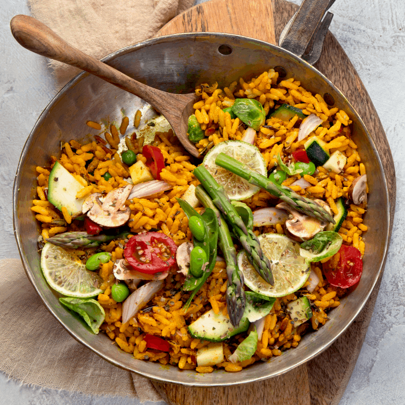 a paella with vegetables and a wooded spoon inside