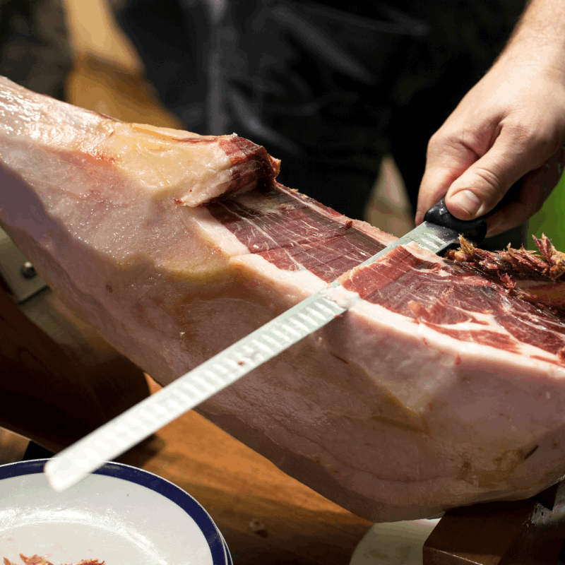 Knife carving a Iberian ham and getting a slice