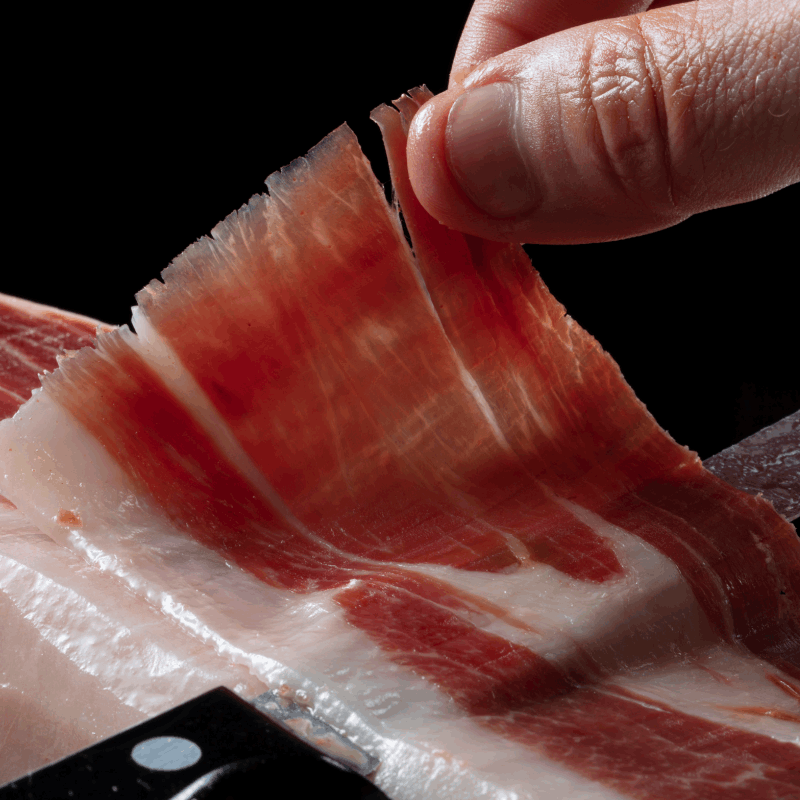 a finger holding a slice of Iberian ham