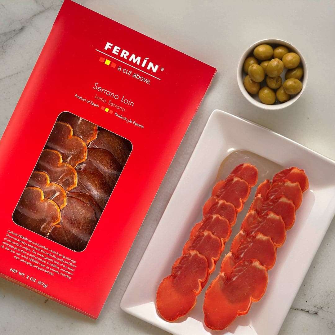 a package of Lomo Serrano Fermin and a plate with sliced Lomo and Olives