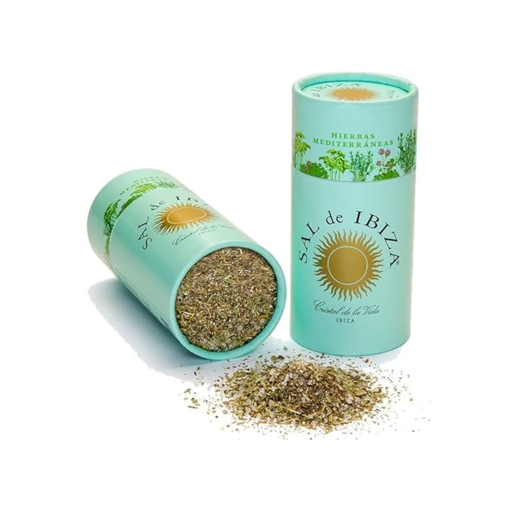 Two teal cylindrical containers of 'Sál de Ibiza' with dried herbs spilling out on a white background.