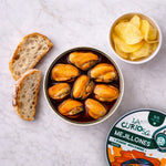 Can of La Curiosa Mejillones with bread and potato chips on a white surface