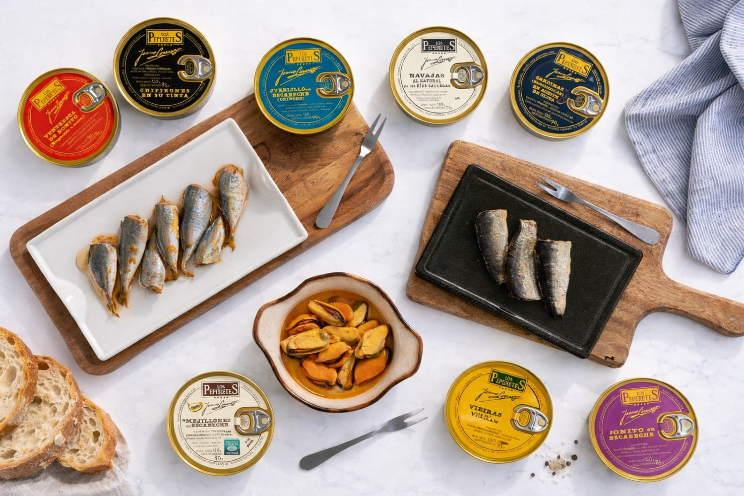 Assorted Spanish tinned fish products on a white surface with wooden cutting boards and bread.