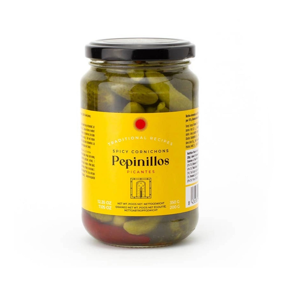 A glass jar of Traditional Recipes Spicy Cornichons Pepinillos (pickled hot peppers) with a bright yellow label and a black lid, set against a plain white background.