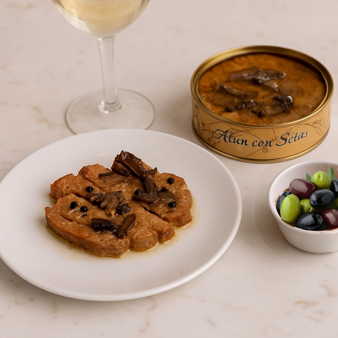Plated dish of atun con setas with a can, glass of white wine, and bowl of grapes on a marble surface.